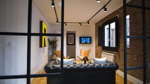 Een moderne woonkamer met een leren zwarte bank, een televisie en een bakstenen muur.