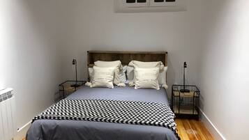 A bedroom with a bed, two bedside tables, a window, and a radiator.