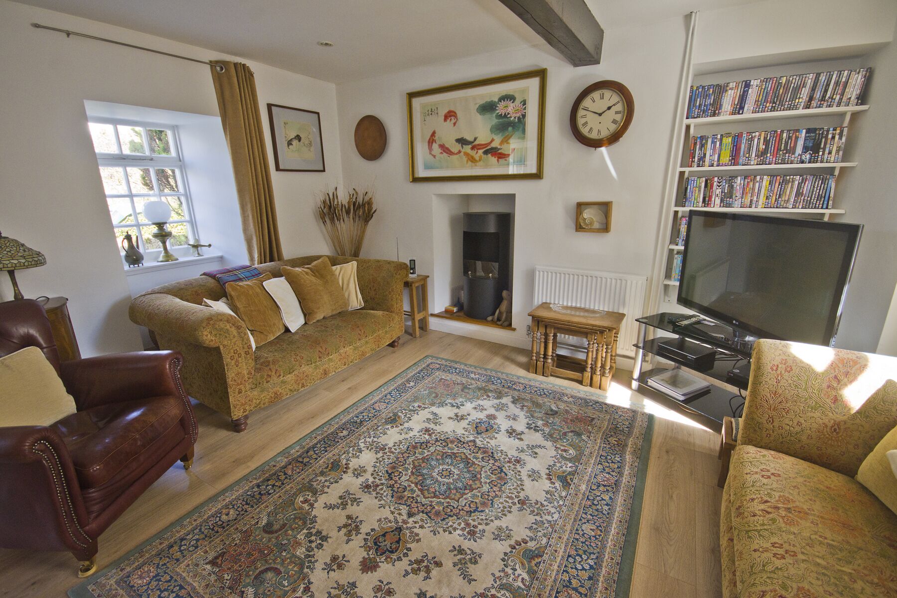 A living room with a sofa, armchair, TV, bookshelf, fireplace, and decorative items.