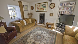 Una sala de estar con sofá, sillón, televisor, estantería, chimenea y objetos decorativos.