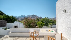 Eine Terrasse mit Tisch und Stühlen, eine weiße Wand und Blick auf Berge.