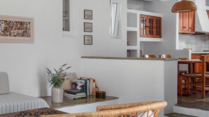 Eine moderne Küche mit Holzausstattung, ein Essbereich mit Korbstühlen und ein Wohnzimmer mit Sofa und Büchern.