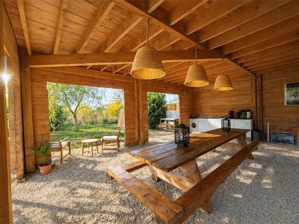 An open-plan wooden cabin with a dining area, kitchen, and outdoor seating.