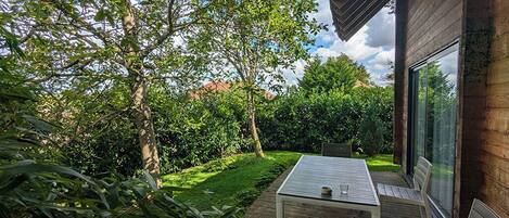 A patio with a table and chairs, surrounded by lush greenery and trees.