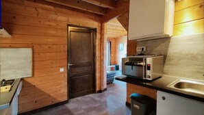 A compact kitchen with wooden walls, a built-in oven, a sink, and a small trash bin.