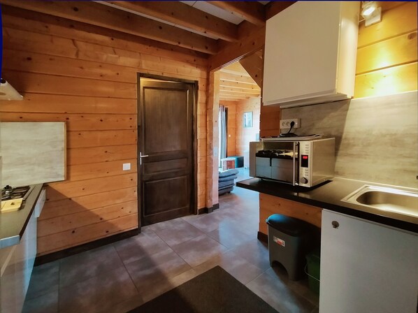A compact kitchen with wooden walls, a built-in oven, a sink, and a small trash bin. - Cottages to Orient - Champagne Chalet (Géraudot)