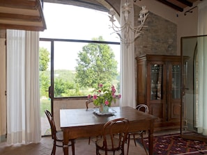 A dining area with a wooden table, chairs, a vase with flowers, a chandelier, and a view of greenery outside. - Country House Nazzano in Vineyards/Olive Grove near San Gimignano Florence Siena (Gambassi Terme)