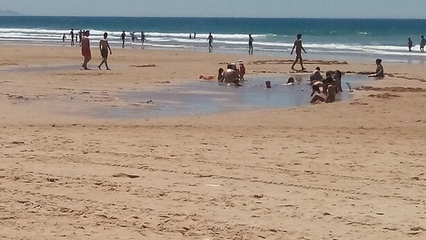 A beach with people walking and playing in the water.