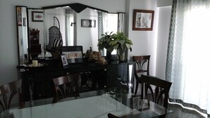 A dining area with a glass table, chairs, a black console table with decorative items, a potted plant, and framed pictures on the wall.
