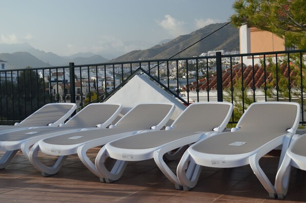 A row of white sun loungers with a view of a mountainous landscape and a building in the background.