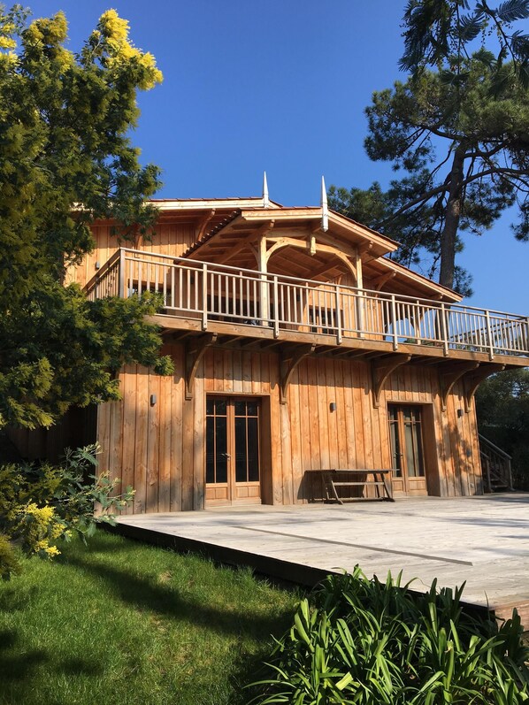 A wooden cabin with a balcony, surrounded by trees and grass.