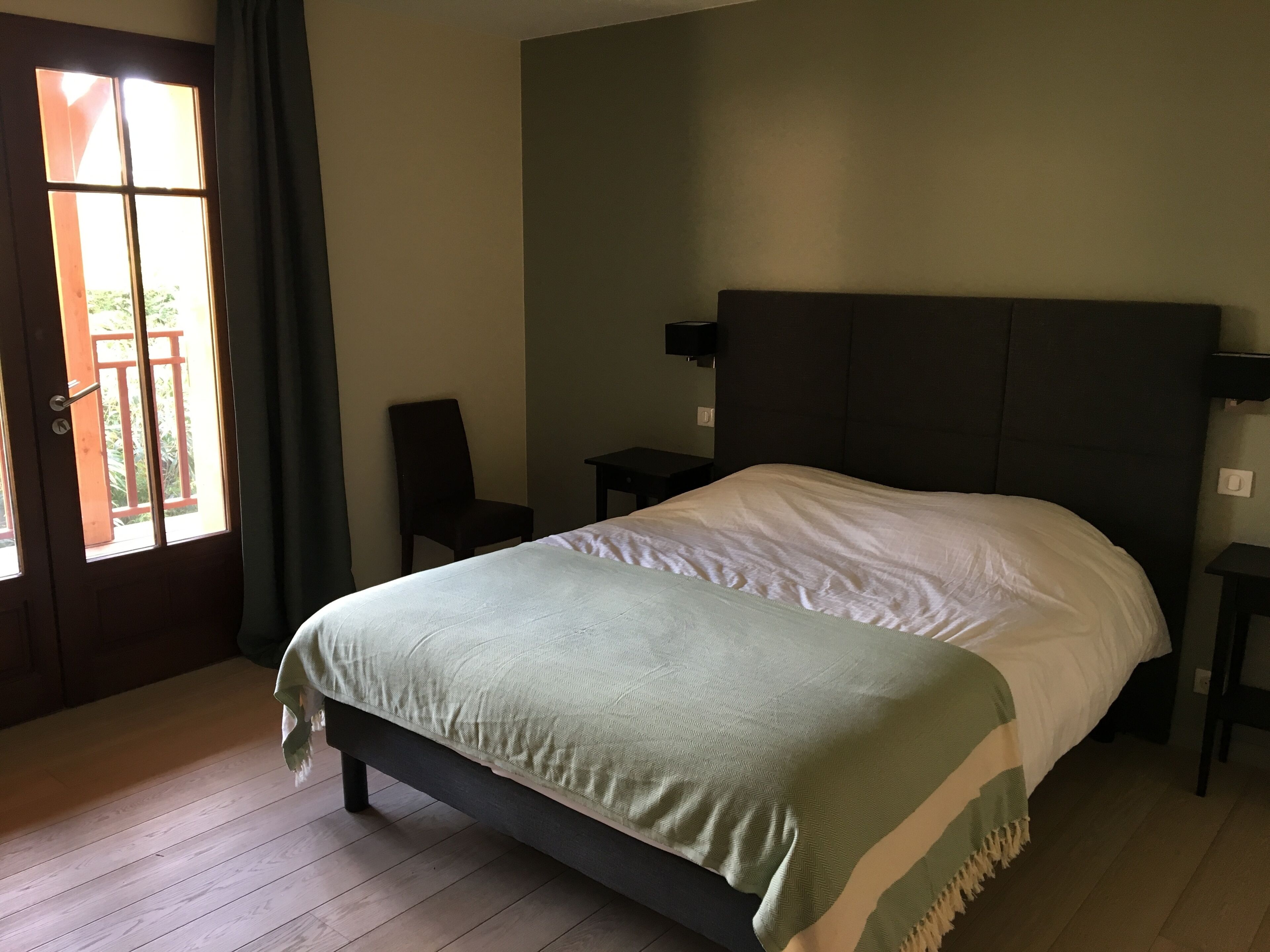 Un dormitorio con cama, una silla, una mesita de noche y una ventana con cortinas.