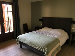 A bedroom with a bed, a chair, a nightstand, and a window with curtains.