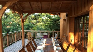 A wooden deck with a table set for four, surrounded by chairs, overlooking a forested area.