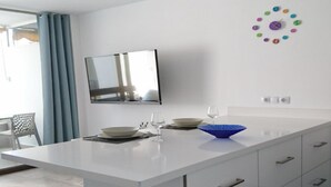 Une cuisine moderne dotée d’un grand îlot central, de meubles blancs et d’un téléviseur à écran plat fixé au mur.