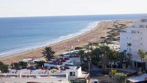 Un hôtel en bord de mer offrant une vue sur la plage, composé de plusieurs bâtiments, agrémenté de palmiers et donnant accès à une plage de sable.