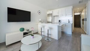 Une cuisine moderne avec des meubles blancs, un îlot central et un téléviseur à écran plat fixé au mur.