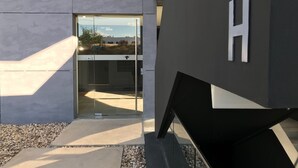 Ein moderner Gebäudeeingang mit Glastür, einem sichtbaren 'H'-Schild und einem Betonweg, der zur Tür führt.