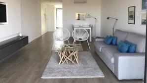 Ein modernes Wohnzimmer mit einem grauen Sofa, zwei weißen Sesseln, einem Glastisch und einem grauen Teppich.