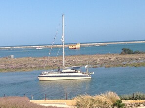 A sailboat anchored near a rocky shoreline with a distant building.