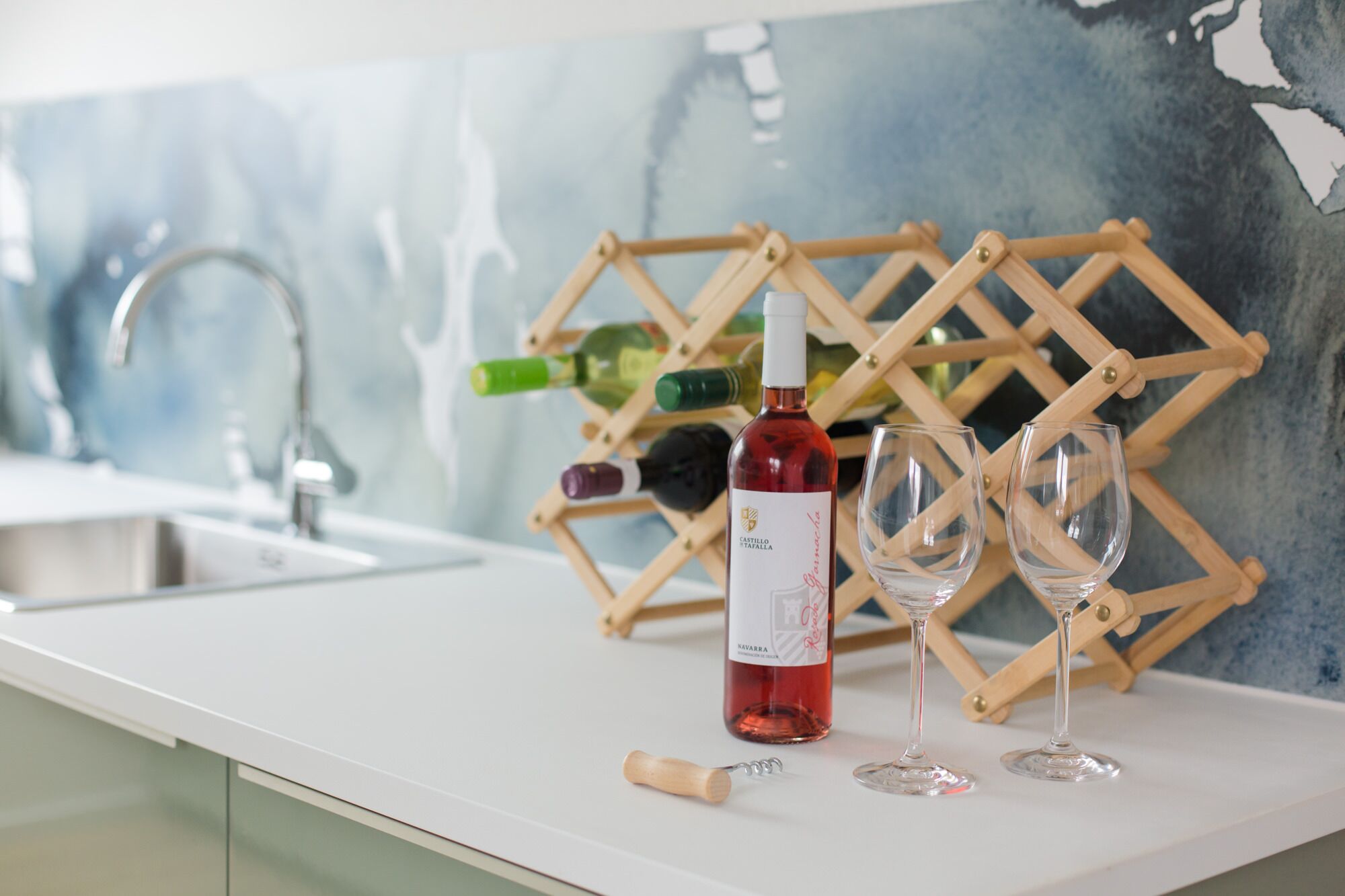 A kitchen counter with a wine bottle, two glasses, and a corkscrew.