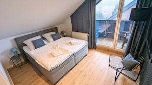Ein Schlafzimmer mit einem großen Bett, einem Sessel, einer Heizung und Blick ins Freie.