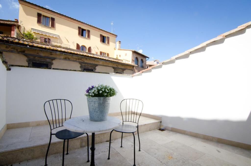 A small outdoor patio with a round table and two chairs, a potted plant, and a white wall.