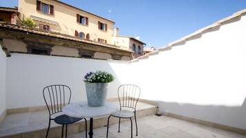 A small outdoor patio with a round table and two chairs, a potted plant, and a white wall.