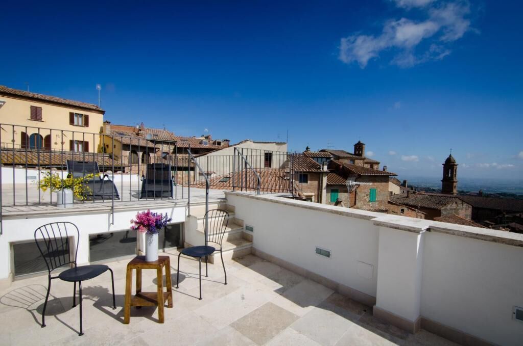 A terrace with a table and chairs, overlooking a town with historic buildings and a church tower.