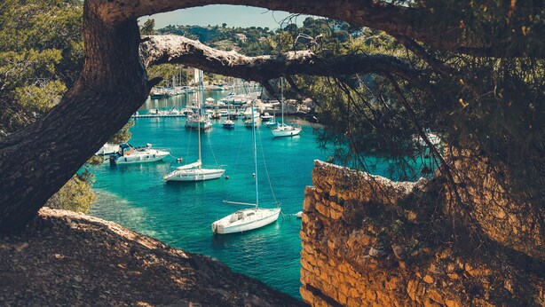 A coastal marina with boats docked, surrounded by rocky terrain and trees.