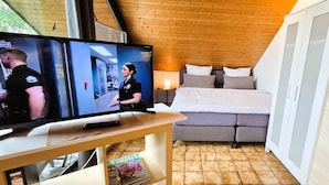 Een moderne kamer met een houten plafond, een bed met grijze beddengoed, een televisie op een houten tafel, en een tijdschrift op de tafel.