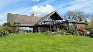 Een modern huis met een schuin dak, grote glasramen en een verzorgde tuin.