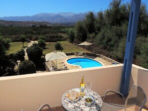 Uma varanda com piscina, mesa com garrafa e copos, e vista para montanhas.