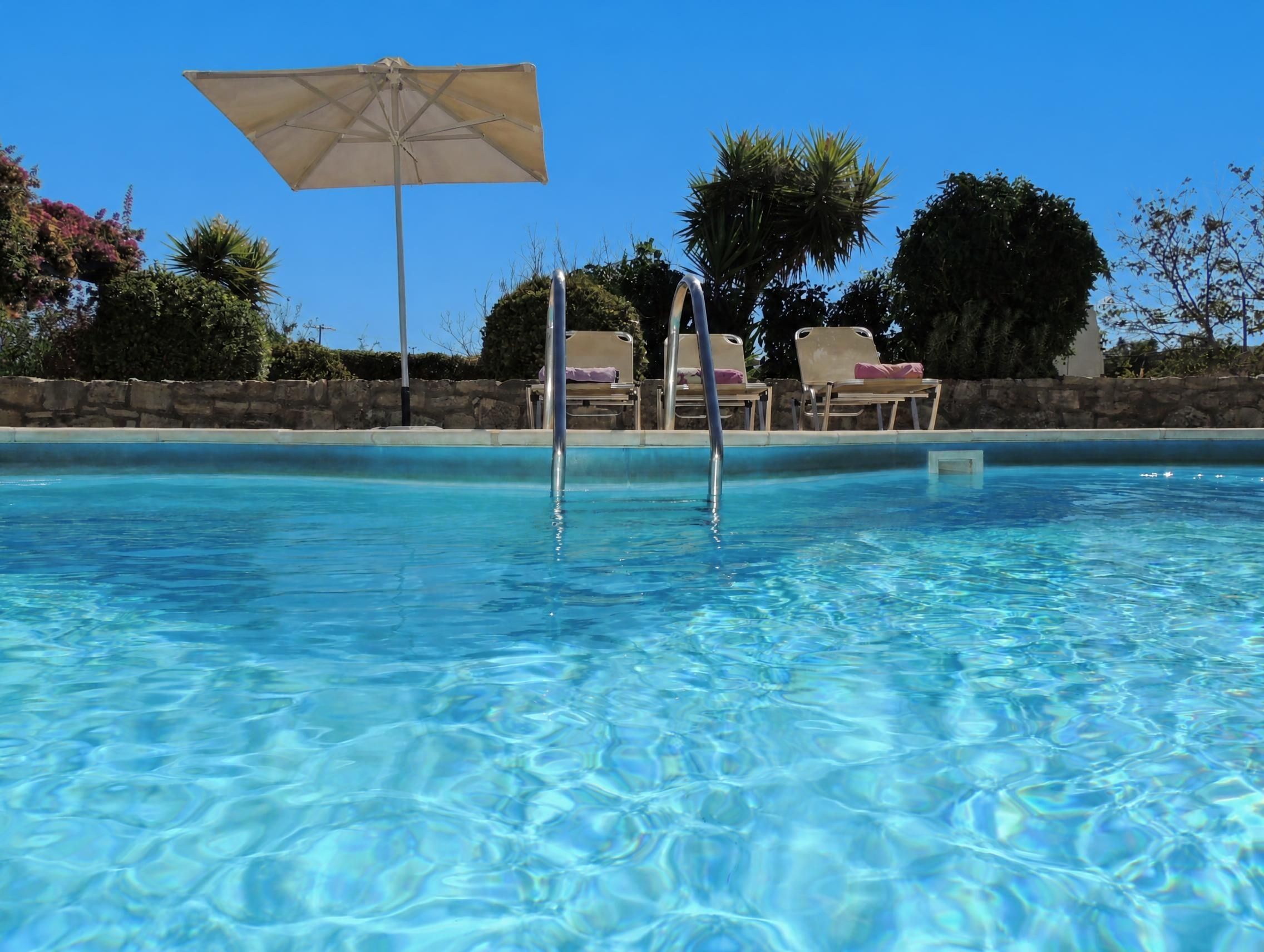 A clear swimming pool with lounge chairs and an umbrella.