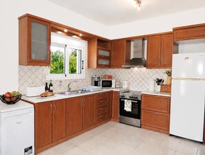 Cozinha moderna com armários de madeira, fogão de aço inoxidável, geladeira branca e janela com vista para o verde.