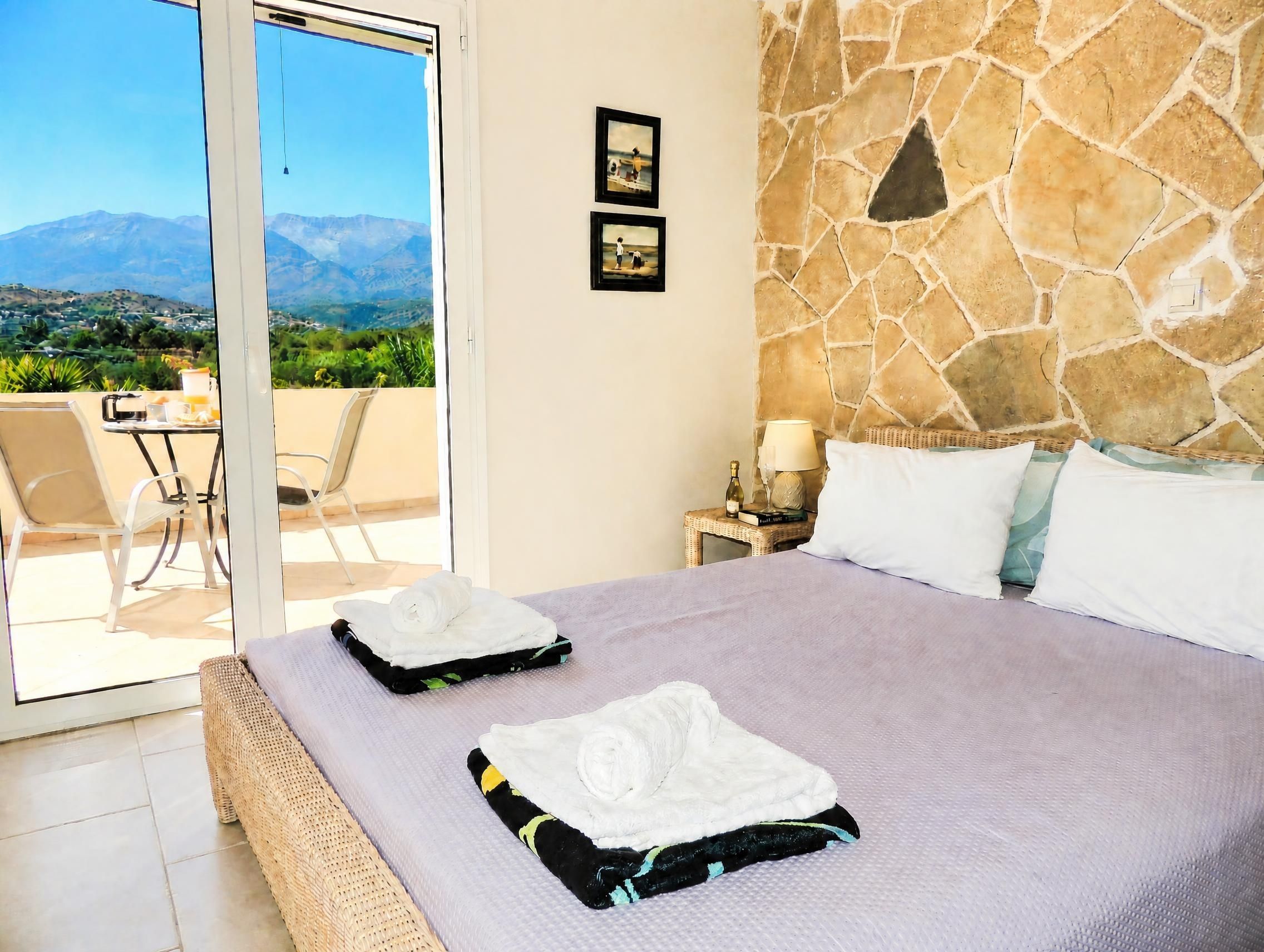 A hotel room with a bed, a table with chairs, a lamp, and a view of mountains.