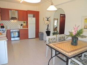 A kitchen with wooden cabinets, a stove, a refrigerator, and a dining area with a table and chairs. - Near Kalives. 2 bedrooms, private pool, Free WIFI, A.C, views and all amenities. (Chania)