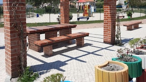 En park med en pergola av tegel, picknickbord och färgstarka blomkrukor.