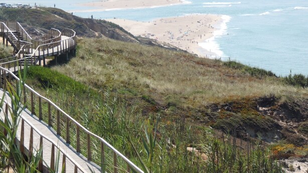 En strandpromenad som leder till en strand, med en trätrappa och ett räcke.