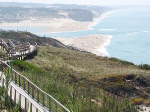 Une promenade en bord de mer menant à une plage, avec un escalier et une rambarde en bois.