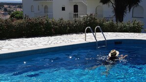 En swimmingpool med kristallklart blått vatten, en vit byggnad med balkonger och en palm på bakgrunden.