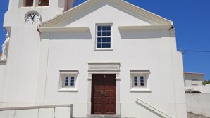 En vit kyrka med en brun dörr, en klocka och ett klocktorn.