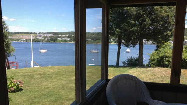 A room with a view of a lake, a chair, and a table.