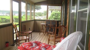 A covered porch with wicker furniture, including a chair with a red cushion and a white wicker chair.