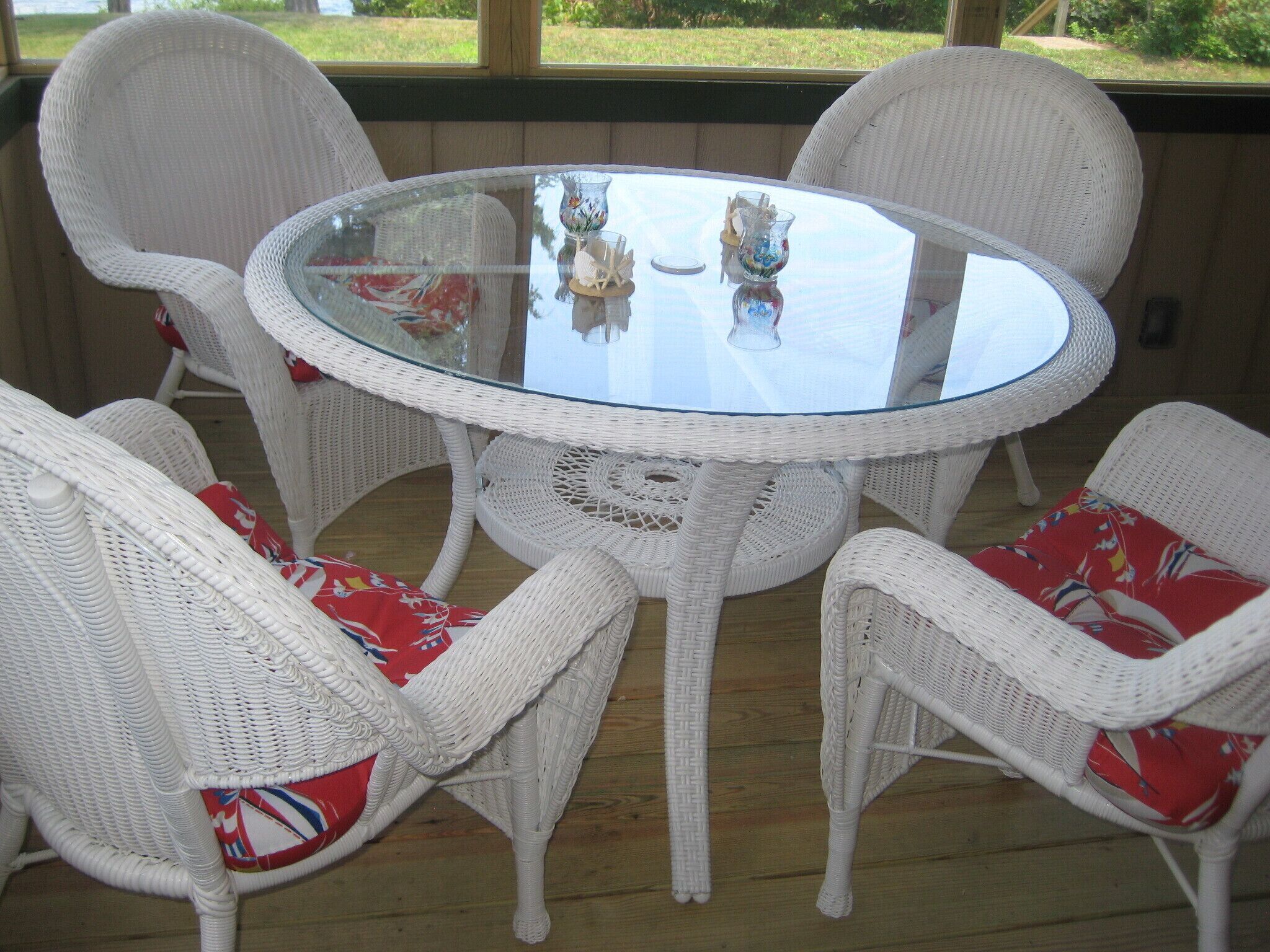A round glass table surrounded by white wicker chairs with red and white patterned cushions.