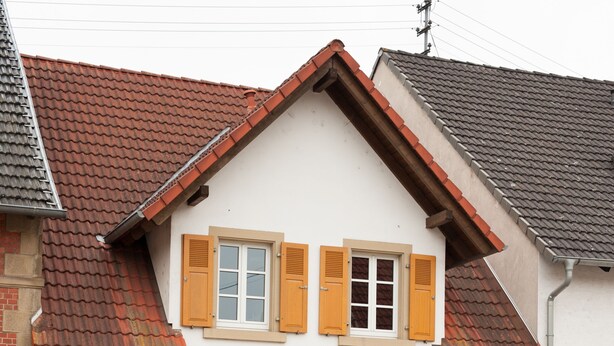 Een huis met twee verdiepingen, een steile kap, houten luiken en een centrale ingang.