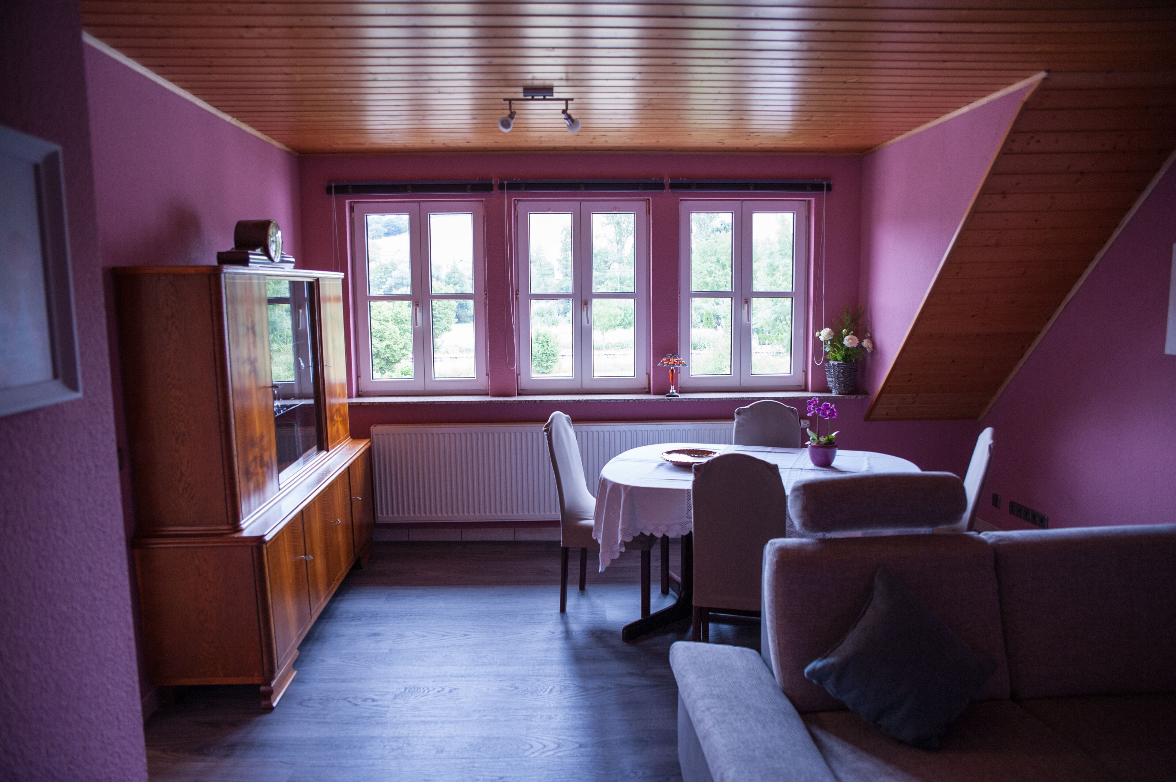 A dining area with a table and chairs, a wooden cabinet, and a window with a view of greenery.