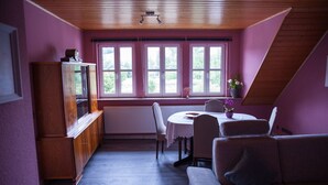 Een eetgedeelte met een tafel, stoelen, een houten kast en een raam met uitzicht op groen.