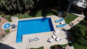 A rectangular swimming pool with a small circular hot tub, surrounded by lounge chairs and a small table.