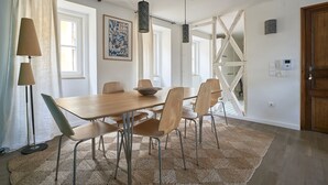 A dining area with a wooden table, six chairs, a woven rug, pendant lights, and a staircase in the background.